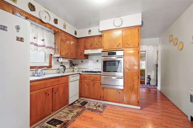 kitchen featuring tasteful backsplash, radiator, white appliances, sink, and light hardwood / wood-style flooring