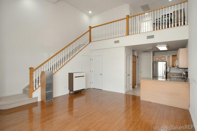 unfurnished living room with a towering ceiling, sink, and light hardwood / wood-style flooring