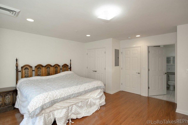 bedroom with hardwood / wood-style flooring, electric panel, and connected bathroom