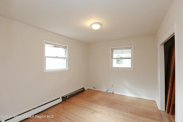 unfurnished room with a baseboard heating unit, hardwood / wood-style flooring, and plenty of natural light