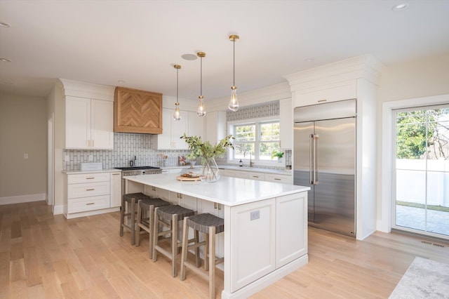 kitchen featuring decorative light fixtures, a center island, white cabinetry, light wood-type flooring, and stainless steel built in refrigerator