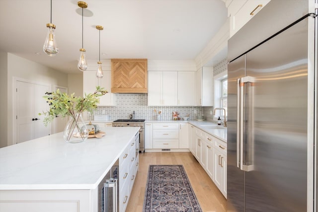 kitchen featuring a center island, sink, high end appliances, hanging light fixtures, and white cabinets