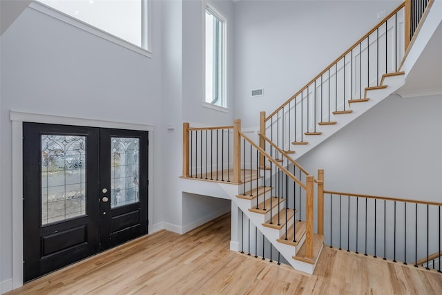 foyer featuring french doors, visible vents, stairway, a towering ceiling, and wood finished floors