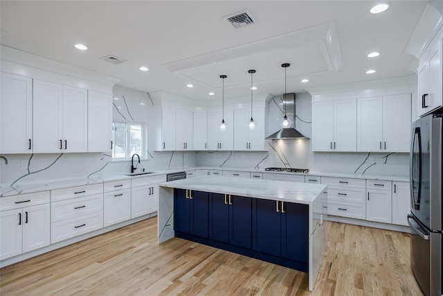 kitchen featuring visible vents, wall chimney range hood, gas cooktop, and freestanding refrigerator