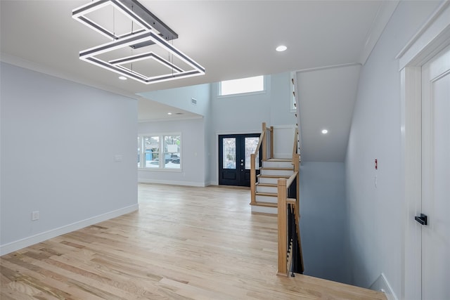 foyer entrance featuring crown molding, light wood finished floors, stairway, and baseboards