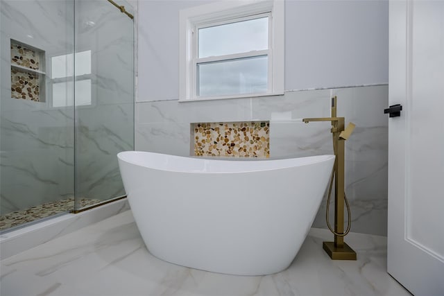 bathroom with marble finish floor, a marble finish shower, a freestanding tub, and tile walls