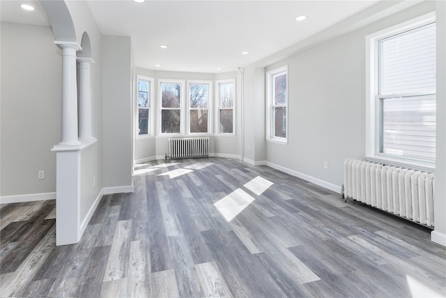 unfurnished living room with dark hardwood / wood-style flooring, radiator heating unit, and ornate columns