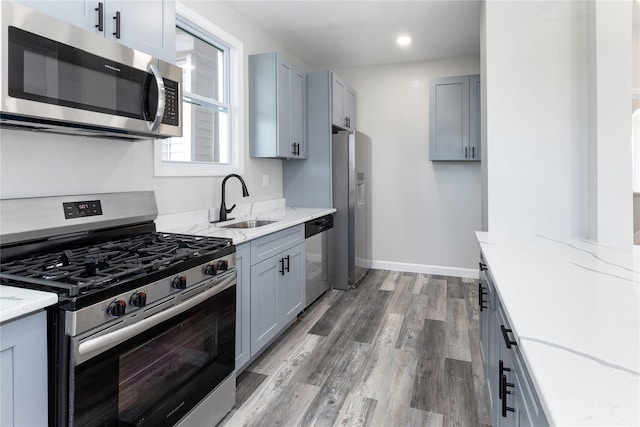 kitchen with sink, dark hardwood / wood-style floors, gray cabinets, light stone countertops, and appliances with stainless steel finishes