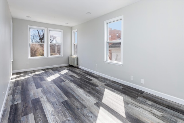 empty room featuring dark hardwood / wood-style floors, radiator heating unit, and a wealth of natural light