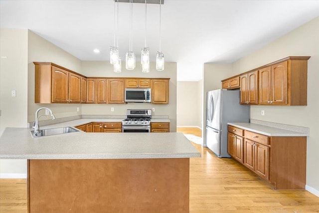 kitchen with hanging light fixtures, sink, appliances with stainless steel finishes, light hardwood / wood-style floors, and kitchen peninsula