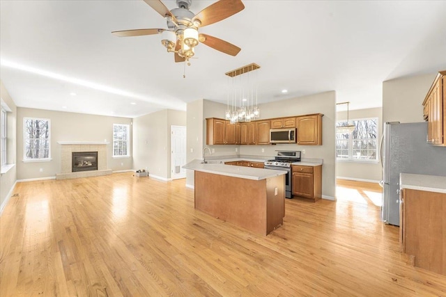 kitchen with ceiling fan with notable chandelier, hanging light fixtures, a fireplace, light hardwood / wood-style floors, and stainless steel appliances