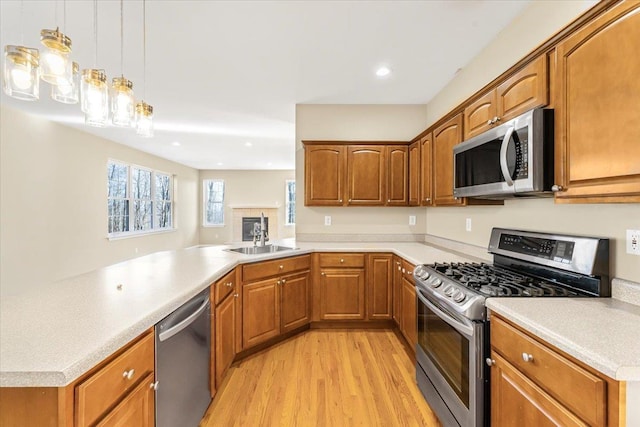 kitchen with sink, stainless steel appliances, kitchen peninsula, decorative light fixtures, and light wood-type flooring