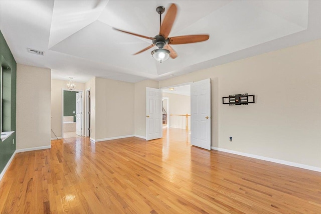 unfurnished room featuring ceiling fan with notable chandelier, a tray ceiling, and light hardwood / wood-style flooring