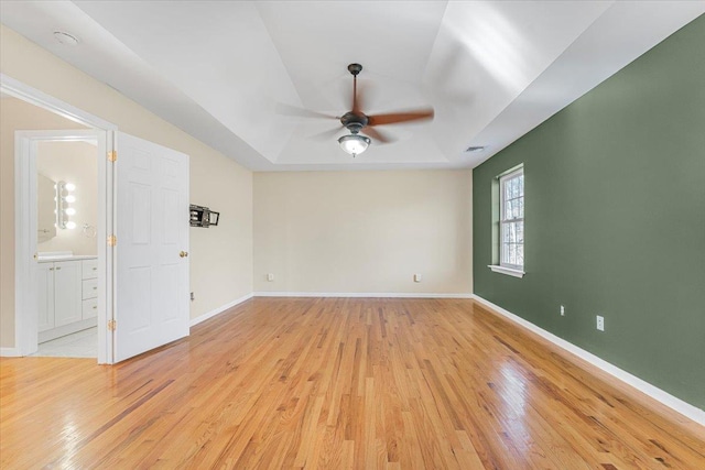 unfurnished room featuring ceiling fan, a raised ceiling, and light hardwood / wood-style flooring