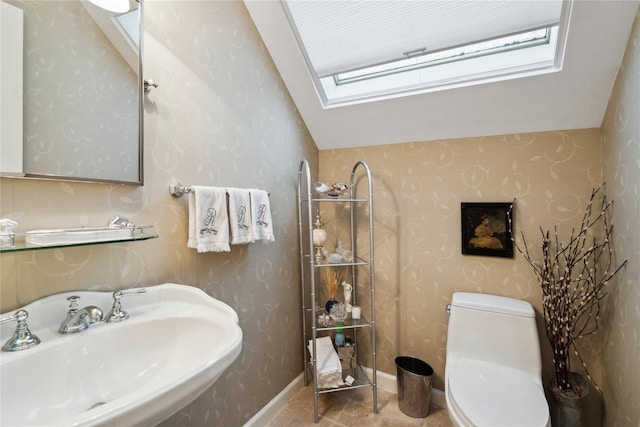 bathroom with tile patterned floors, lofted ceiling with skylight, sink, and toilet