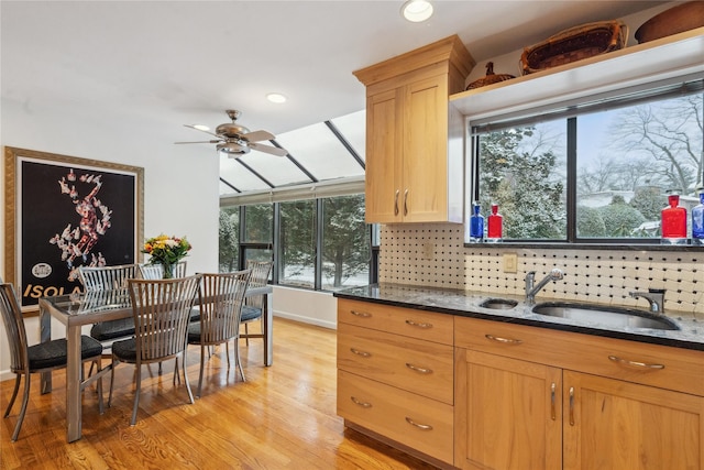 kitchen featuring dark stone counters, sink, ceiling fan, decorative backsplash, and light hardwood / wood-style floors