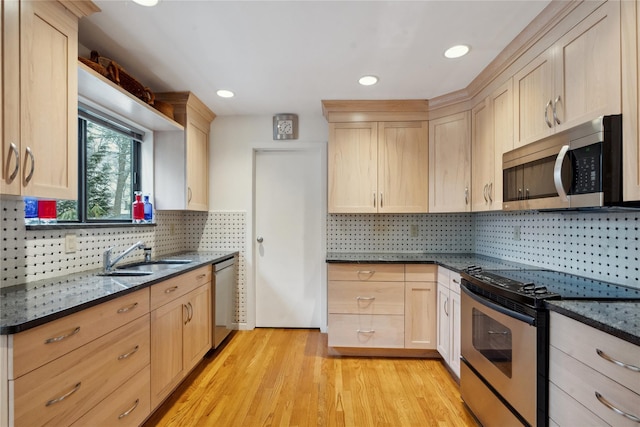 kitchen featuring appliances with stainless steel finishes, light wood-type flooring, light brown cabinetry, dark stone counters, and sink