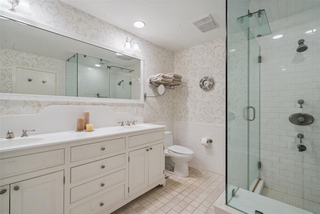 bathroom with tile patterned flooring, toilet, a shower with door, vanity, and tile walls