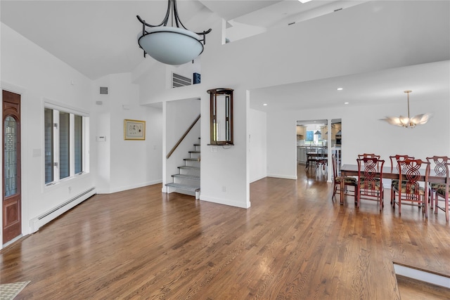 dining area featuring a chandelier, wood-type flooring, a towering ceiling, and baseboard heating