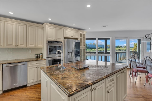 kitchen with appliances with stainless steel finishes, a center island with sink, dark stone counters, and sink