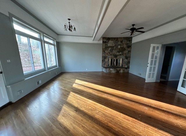 unfurnished living room with ceiling fan with notable chandelier, dark hardwood / wood-style floors, and a stone fireplace