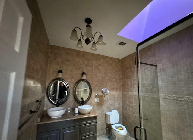 bathroom with vanity, toilet, a shower with door, and tile walls