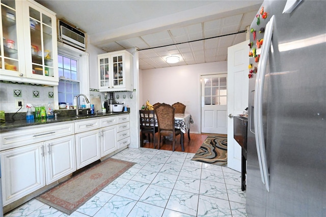 kitchen featuring white cabinetry, sink, stainless steel fridge with ice dispenser, backsplash, and dark stone counters