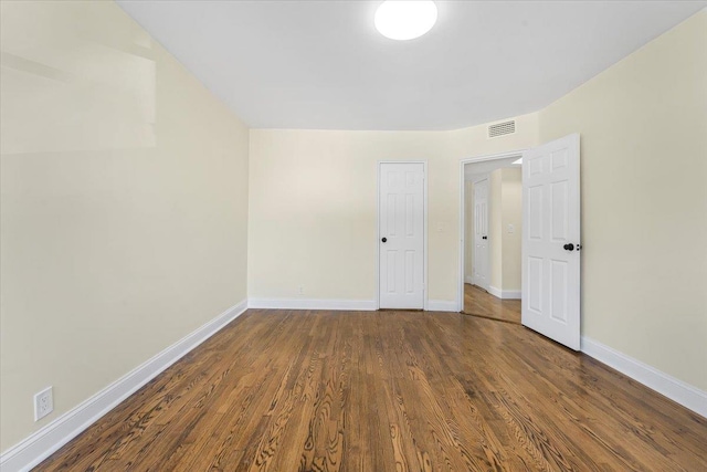 empty room with dark wood-type flooring, visible vents, and baseboards