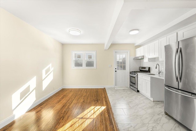 kitchen with a sink, light countertops, under cabinet range hood, appliances with stainless steel finishes, and marble finish floor