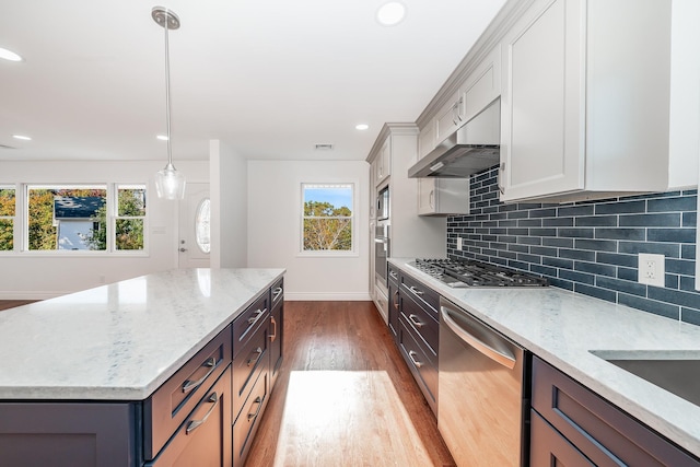 kitchen featuring backsplash, light stone counters, ventilation hood, stainless steel appliances, and decorative light fixtures