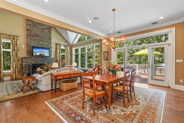 dining space featuring an inviting chandelier, crown molding, a fireplace, and light hardwood / wood-style flooring