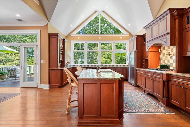 kitchen featuring sink, a breakfast bar area, light stone counters, stainless steel appliances, and a kitchen island with sink