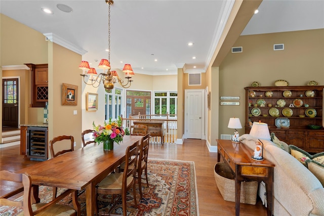 dining area with crown molding, an inviting chandelier, wine cooler, and light hardwood / wood-style floors