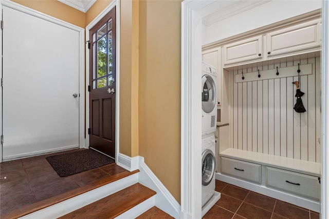 mudroom featuring crown molding, stacked washer / dryer, and dark tile patterned flooring