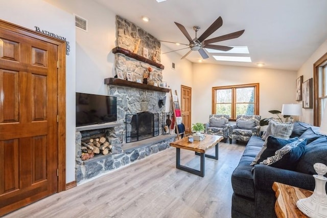 living room featuring vaulted ceiling with skylight, ceiling fan, a fireplace, and light hardwood / wood-style flooring