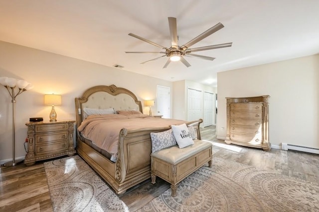 bedroom with ceiling fan, baseboard heating, dark wood-type flooring, and a closet