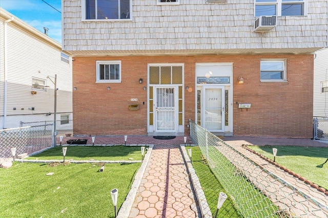 view of exterior entry with mansard roof, fence, and brick siding