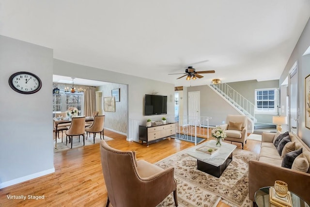 living room featuring stairs, ceiling fan with notable chandelier, light wood-type flooring, and baseboards