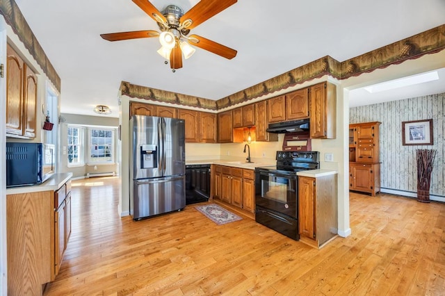 kitchen with wallpapered walls, under cabinet range hood, light countertops, black appliances, and a sink