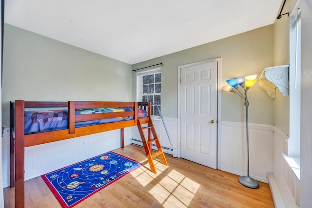 bedroom with a baseboard heating unit, wainscoting, and wood finished floors