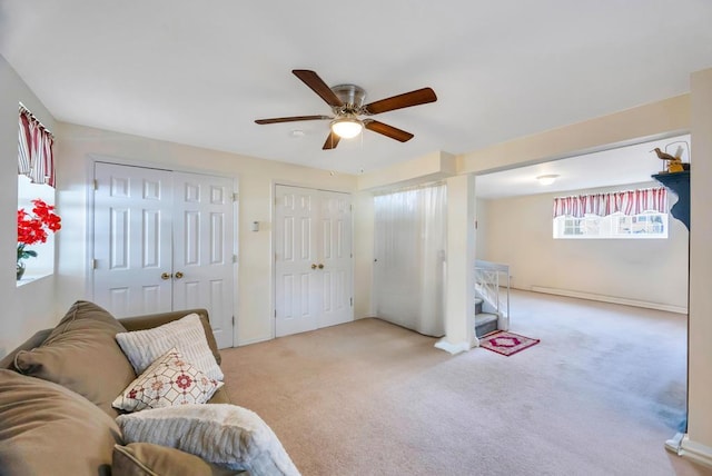 living area featuring a ceiling fan, light colored carpet, and stairs