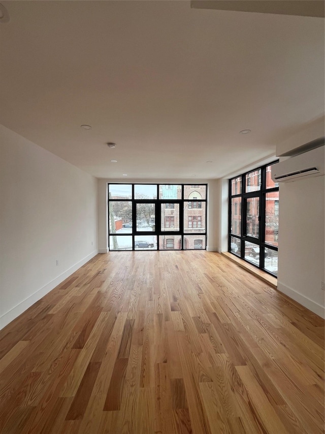 spare room with floor to ceiling windows, a wall mounted AC, and light hardwood / wood-style floors