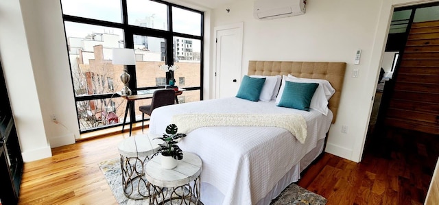 bedroom featuring wood finished floors, baseboards, and a wall mounted AC