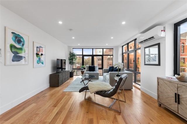 living room featuring an AC wall unit, baseboards, recessed lighting, and light wood-type flooring