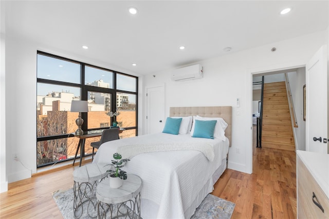bedroom featuring light wood-style flooring, an AC wall unit, recessed lighting, and expansive windows