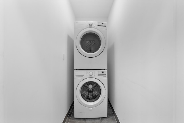 clothes washing area featuring laundry area, baseboards, tile patterned floors, and stacked washer / dryer