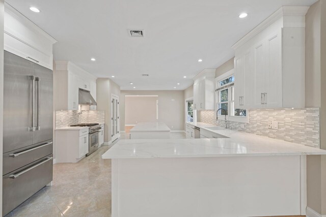 kitchen with white cabinets, kitchen peninsula, premium appliances, and sink