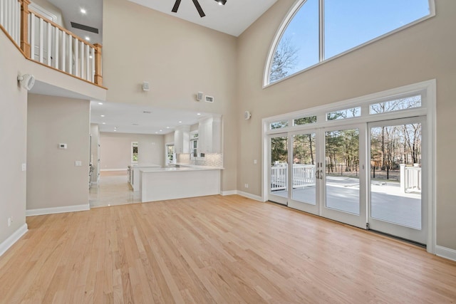 unfurnished living room featuring ceiling fan, a towering ceiling, and light hardwood / wood-style flooring