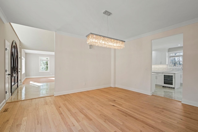 unfurnished dining area featuring wine cooler, an inviting chandelier, crown molding, and light hardwood / wood-style flooring