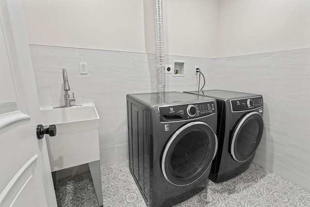 clothes washing area with light tile patterned floors, tile walls, and washer and dryer